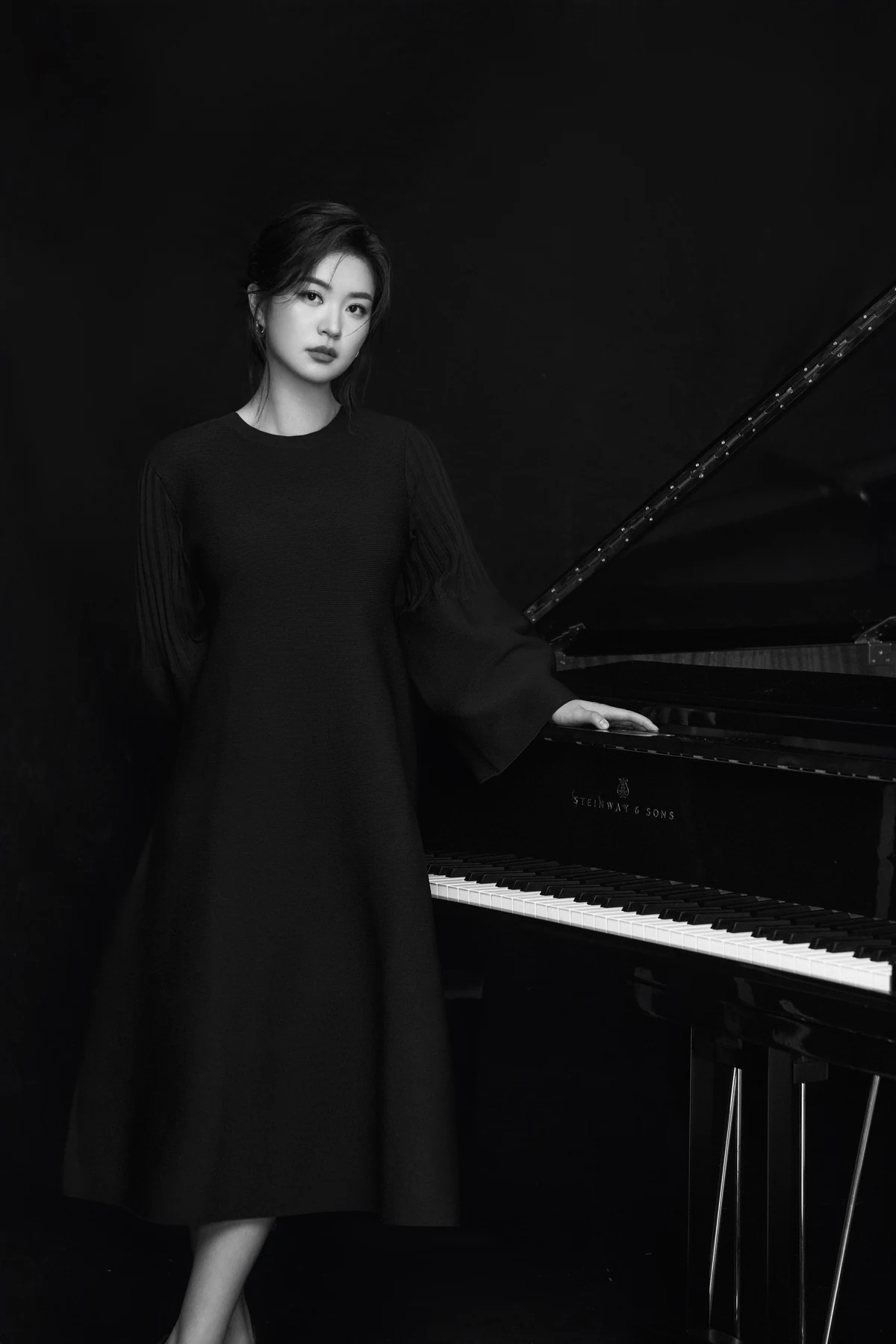 Ming Hu standing beside a Steinway grand piano, photographed in black and white